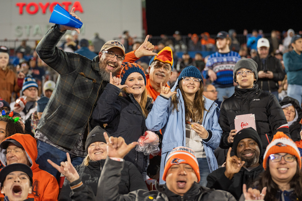 A group of people giving the "Birds Up" hand sign while cheering at a football game